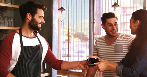 Smiling waiter serving happy couple fresh coffee in charming cafe