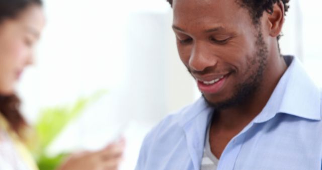 Man smiling while using a smartphone in a bright, modern indoor environment. Ideal for representing technology, modern lifestyle, communication, casual work, and everyday tech use.