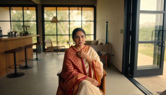 Elegant woman wearing cream saree and red-gold shawl sitting and gazing in modern living room
