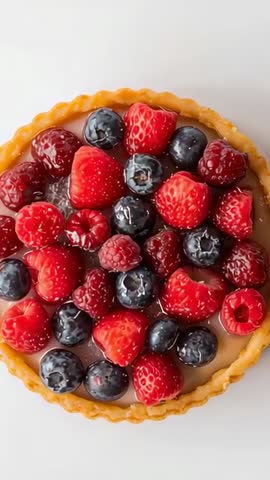 Camera gliding over glossy mixed berry caramel tart close-up top-down vertical video