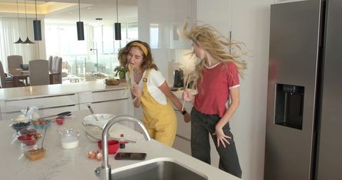 Friends singing and dancing in modern sunlit kitchen with baking ingredients on island