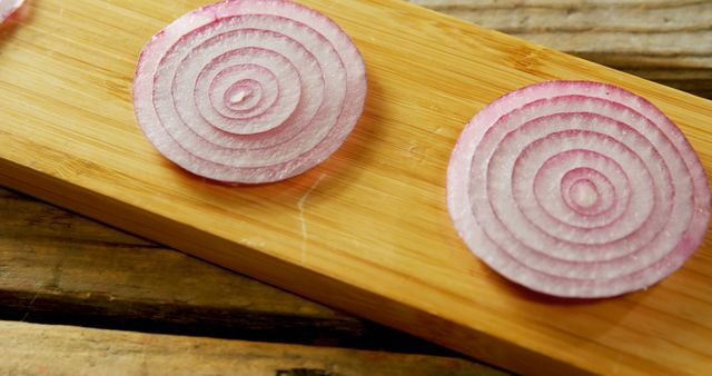 Sliced red onion rings rest on a wooden cutting board, with copy space. Their vibrant purple layers add a pop of color and hint at the flavorful addition they can make to various dishes.