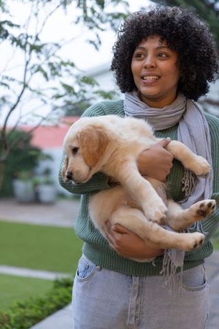 Smiling woman holding golden retriever puppy in backyard garden casual lifestyle portrait