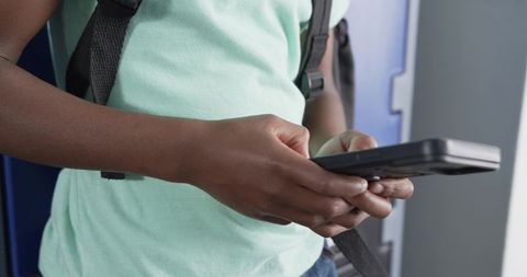 African american teen holding calculator and checking homework by school lockers