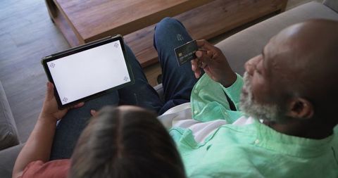 Senior couple completing online payment with tablet and credit card on sofa