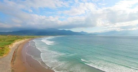 Sunlit turquoise seaside with sandy shoreline, rolling dunes and walking couple