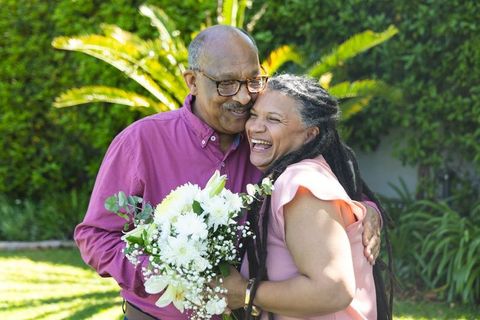 Sunlit african american couple embracing, laughing, sharing white bouquet in backyard