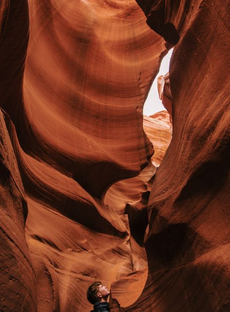 Tourist marveling at the impressive curves of Antelope Canyon's sandstone rock formations. Ideal for use in travel guides, adventure articles, nature tourism promotions, and geological study materials. Perfect visuals for showcasing natural wonders and inspiring outdoor adventures.