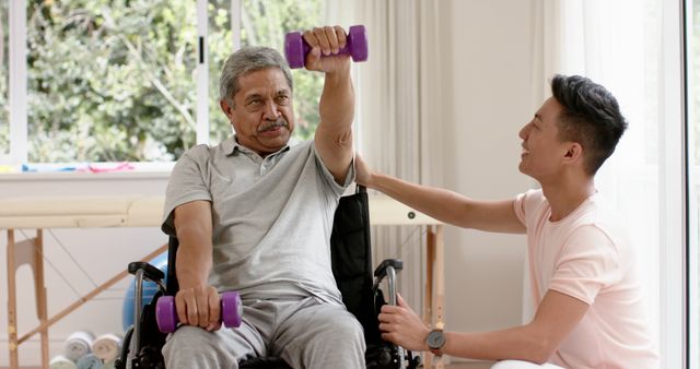 Caregiver assisting elderly man in wheelchair with resistance band exercise at home. Ideal for use in articles on elderly care, physical rehabilitation, and in-home health support. Helpful for promoting health services, fitness programs for seniors, and caregiver support resources.