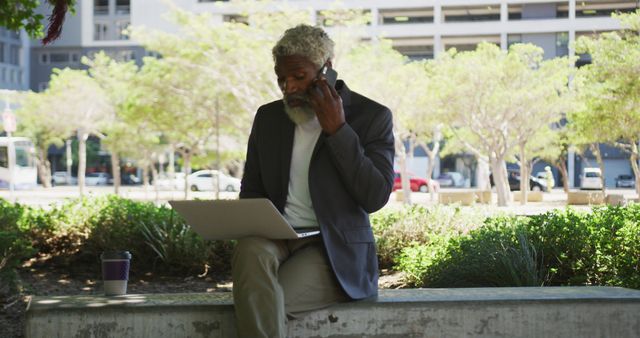 African american senior man talking on smartphone while using laptop in corporate park - Download Free Stock Photos Pikwizard.com