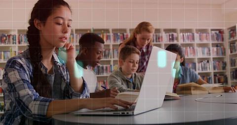 Students Collaborating at Round Library Table with Laptop, Notebooks and Open Books
