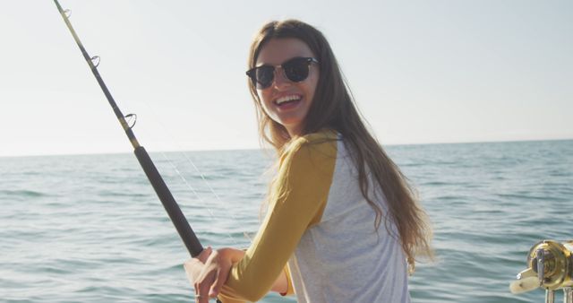 Portrait of happy caucasian teenage girl fishing from deck of a boat in the ocean on a sunny day. Leisure, hobbies, free time, travel and vacations.