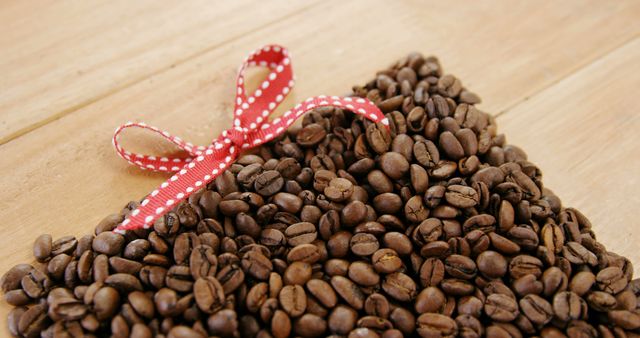 A red ribbon with white polka dots is tied around a pile of roasted coffee beans, with copy space. Coffee beans are often associated with energy and the ribbon suggests a gift or a special presentation of the beans.