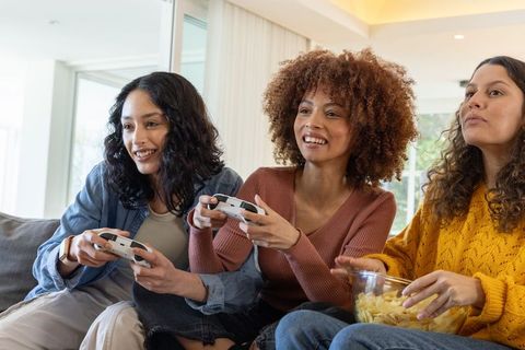 Friends gaming night at home playing console games, laughing, snacking on chips