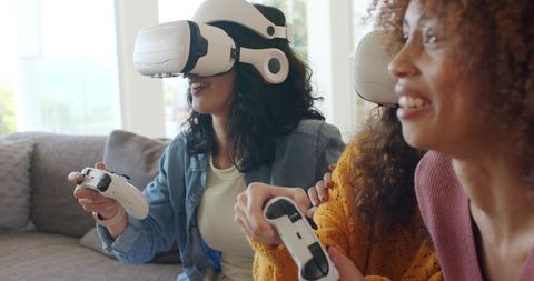 Friends wearing VR headsets holding controllers on couch enjoying social virtual gaming