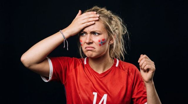 Frustrated norwegian football fan grimacing holding head wearing red jersey number 14