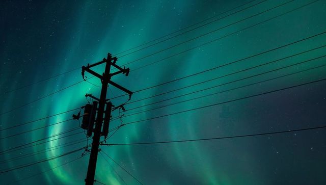 Silhouetting utility pole and power lines under vibrant northern lights and starry sky