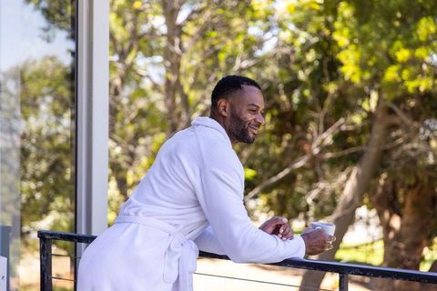African american man in white bathrobe relaxing with morning coffee on sunlit balcony