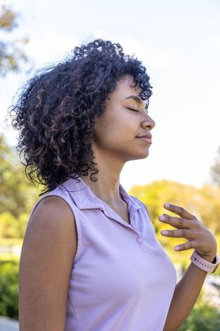 African american woman breathing deeply with eyes closed in sunlit park, serene profile