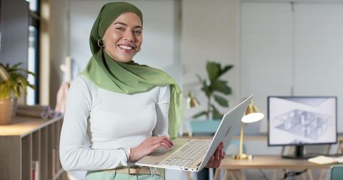 Indian professional woman in green hijab holding laptop presenting architectural blueprint