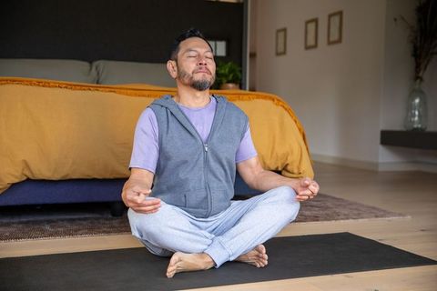 Mature asian man meditating on yoga mat in minimalist bedroom embracing calm and mindfulness