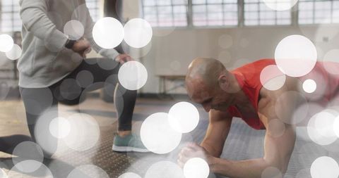 Male athlete holding forearm plank while trainer watches during intense gym workout