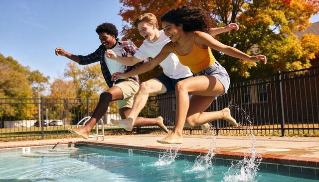 Three teens jumping into pool on autumn day splashing water laughing together