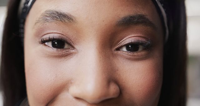 This image shows a close-up of a young African American woman's eyes and upper face, highlighting her eyeliner, natural makeup, and subtle facial expression. Her hair is held back by a headband. Ideal for use in advertisements for beauty products, skincare, personal care items, and any campaigns promoting confidence and natural beauty.