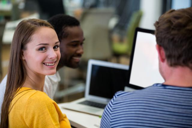 Female graphic designer smiling at camera while colleagues interacting with each other in office