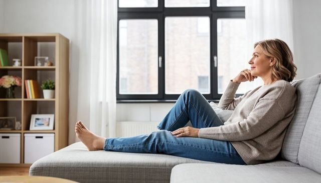 Mature woman relaxing on sofa by window in cozy neutral minimalist living room