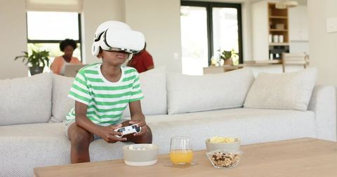 African American child playing VR headset on sofa with parents relaxing in living room