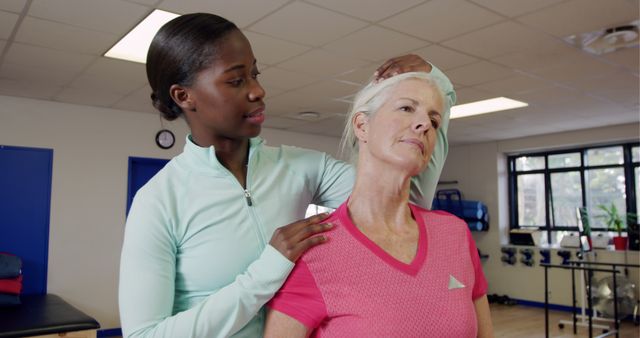 Physical therapist assisting elderly woman during rehabilitation session in a clinic background. Ideal for use in healthcare, physical therapy, elderly care services, recovery programs, and medical practice promotions.