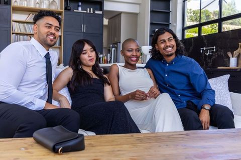 Diverse friends smiling and relaxing on white sofa in modern open-plan living room