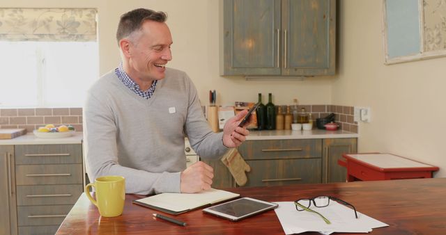 Smiling Man Using Smartphone with Notebook and Tablet in Kitchen - Download Free Stock Images Pikwizard.com