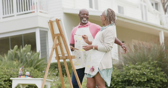Happy senior african american couple painting picture in garden and laughing. Retirement, togetherness, creativity, hobbies and senior lifestyle, unaltered.