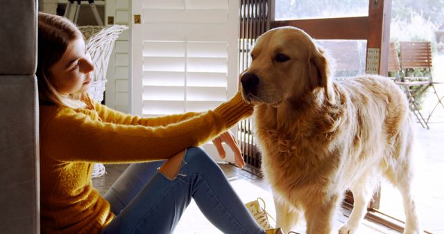 Young woman is bonding with her golden retriever indoors. Both appear relaxed and comfortable. This can be used to portray pet companionship, indoor relaxation, and human-animal bonds. Good for blogs on pet care, social media posts about pets, or articles on how pets improve our lives.