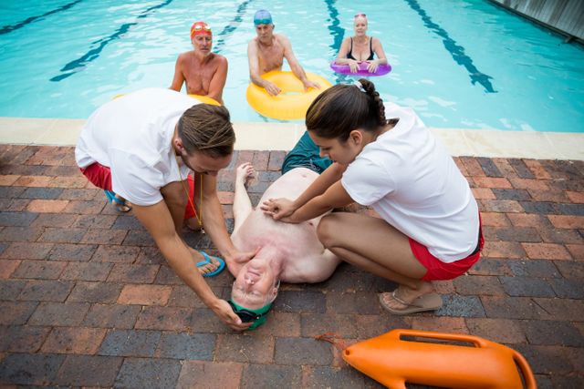 Rescue workers are providing first aid to an unconscious senior man by the poolside. This image can be used for articles or materials related to water safety, lifeguard training, emergency response, elderly care, and health and safety protocols.