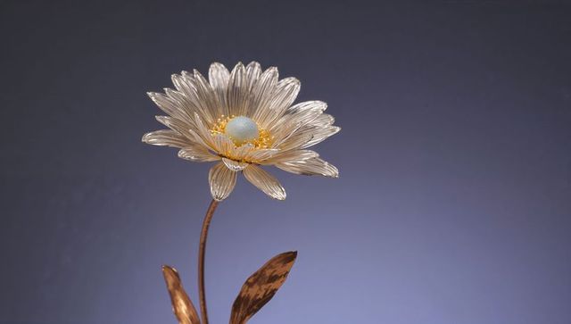 Metallic daisy sculpture with polished copper stem and glowing golden center on blue-gray