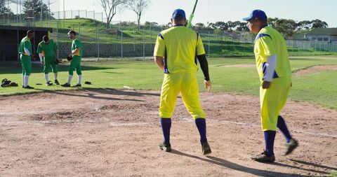 Community baseball team warming up and chatting on sunny infield in contrasting uniforms