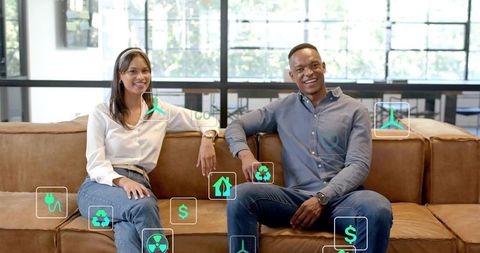 Smiling coworkers sitting on office lounge couch using sustainability and energy holograms
