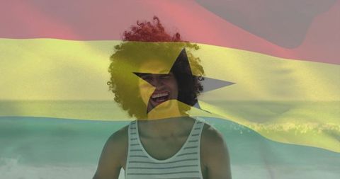 Laughing young man with curly hair standing on shoreline with ghana flag overlay