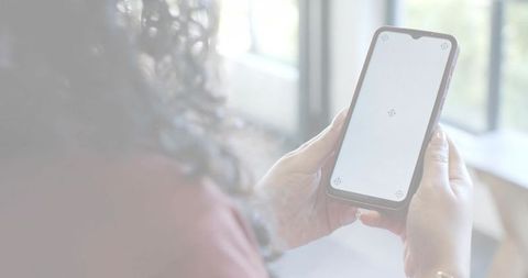 Woman holding smartphone with blank screen mockup near window, bracelet visible