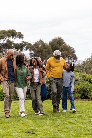 Multigenerational african american family walking through green park wearing cozy sweaters