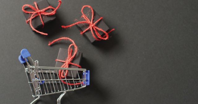 Three black gifts tied with red string and shopping cart on black background with copy space. Black friday, shopping, sale and retail concept digitally generated image.