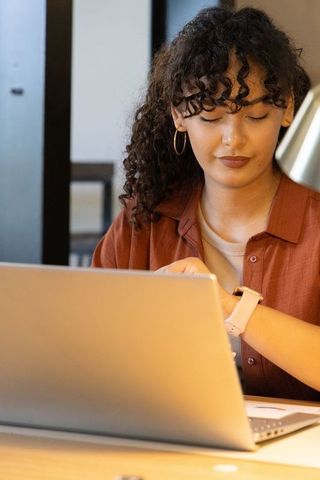 Young woman checking smartwatch while working on laptop in modern coworking workspace