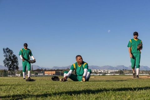 Multicultural Baseball Team Stretching and Warming Up on Outfield Grass with Gloves