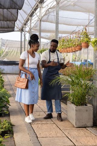 African american plant expert guiding customer through greenhouse nursery consultation