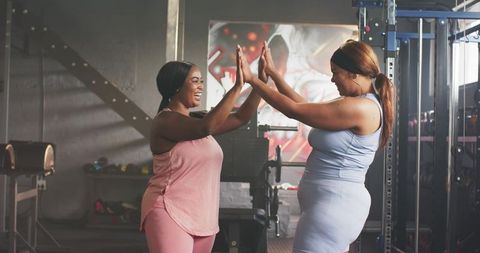 Diverse mid-adult women high-fiving in gym celebrating fitness progress and friendship