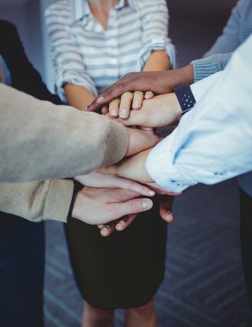 Business colleagues stacking hands in a show of unity and teamwork. Ideal for illustrating concepts of collaboration, support, and partnership in a corporate setting. Useful for business presentations, team-building workshops, and motivational materials.
