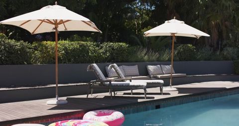 Sunlit poolside retreat with white parasols and chaise lounges on timber deck